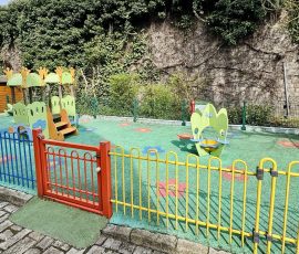 Notre jardin sécurisé : un espace extérieur pour profiter de l'air frais, grimper, glisser et s'épanouir en plein air. Aire de jeux extérieure de la crèche Petit-à-Petit à Douai avec sol souple antichoc, jeux de motricité colorés, clôtures de sécurité et cabane en bois adossée à un mur végétalisé.